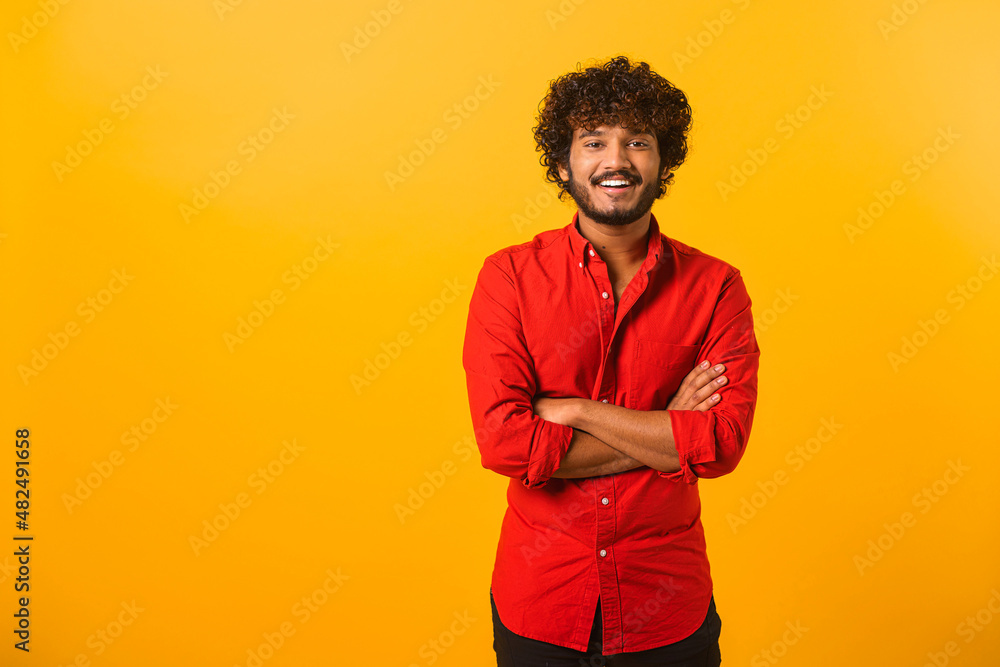 Portrait of happy satisfied handsome young man in shirt standing with crossed arms and looking at camera with toothy smile. Indoor studio shot on orange background Portrait of happy satisfied handsome young man in shirt standing with crossed arms and looking at camera with toothy smile. Indoor studio shot on orange background