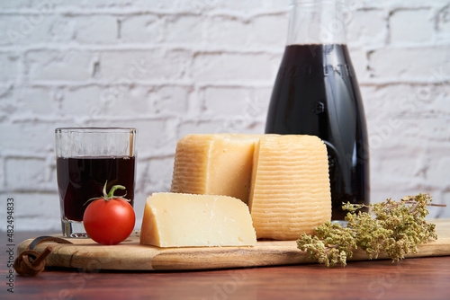 Italian hard cheeses such as pecorino or caprino, Italian wine with carafe and traditional glass, tomato and oregano. Sliced ​​cheese with a bunch of oregano on a wooden board.