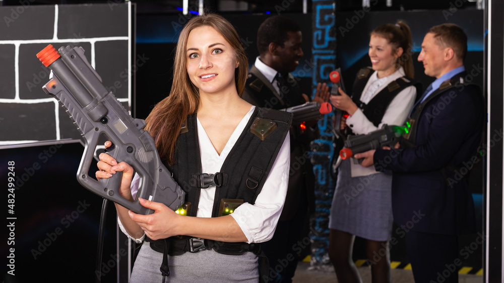 Emotional portrait of woman playing laser tag with her co-workers on dark arena
