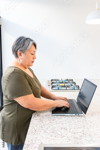 Senior adult woman working from her home kitchen. old woman enjoying videos