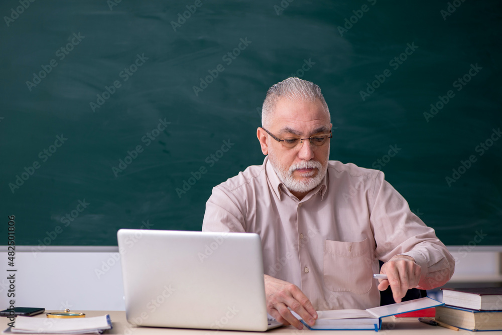 Old male teacher in front of blackboard Old male teacher in front of blackboard