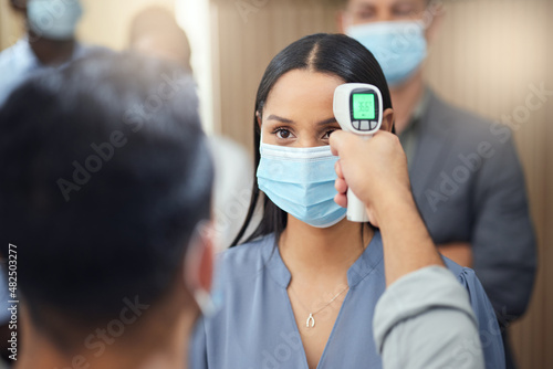 Let me just get your temperature. Cropped shot of an attractive young businesswoman wearing a mask and having her temperature taken while standing at the head of a queue in her office.