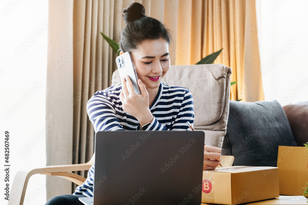 Online merchandising business idea, beautiful girl talking on the phone and holding a parcel box ready to use a computer to enter the Track And Trace parcel number to the customer. Online merchandising business idea, beautiful girl talking on the phone and holding a parcel box ready to use a computer to enter the Track And Trace parcel number to the customer.