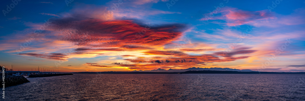 A panorama with Colorful clouds and an overcast sky at sunset with the ocean in the foreground and mountains in the background