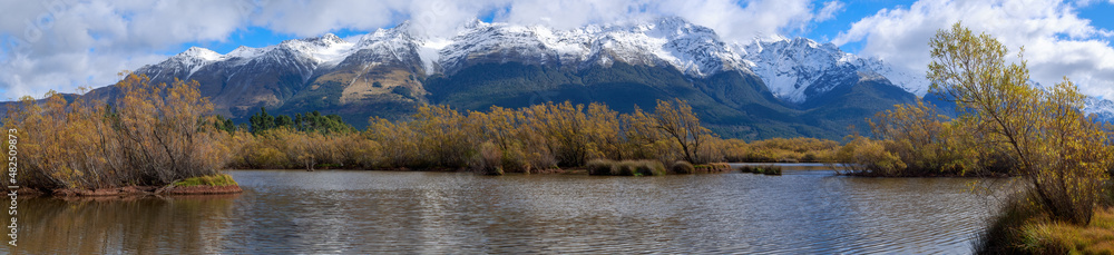Panoramic view of autumn willow trees in the Glenorchy Lagoon, a wetland in Otago, New Zealand. In the background are the snow-capped Humboldt Mountains