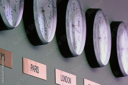 Row of various time zone clocks with placard text on wall at office photo