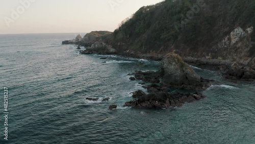 Aerial orbit shot of a big rock formation on the coastline of Zipolite, Oaxaca, Mexico on a cloudy day. photo