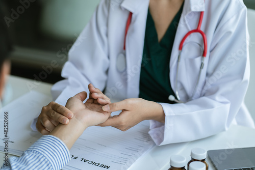 Woman doctor talks to female patient in hospital office while examining the patients pulse by hands. Healthcare and medical service.