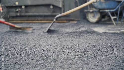 Paving laborers leveling fresh asphalt on a road construction site using asphalt lutes with one of them loading a wheelbarrow in the background. photo