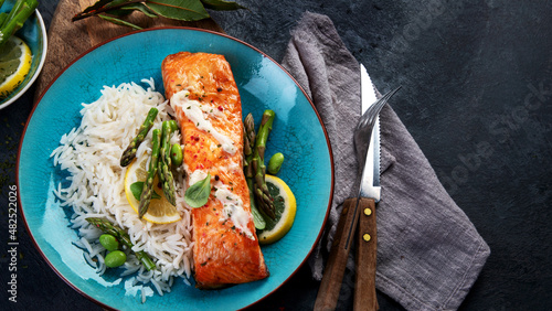 Baked salmon with rice and asparagus on gray background.