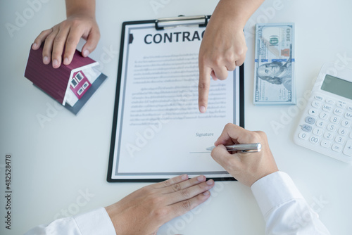 A real estate agent with a house model is talking to clients about buying home insurance and having customers sign contracts under the formal contract agreement. Home rental and insurance concept
