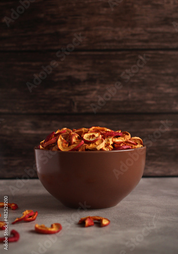 dried apple slices in a brown dish on a dark wooden background