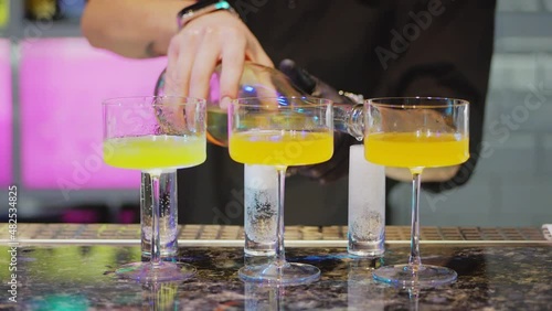 The bartender prepares a colorful cocktail by pouring a drink from a shaker into three glass cremans. photo