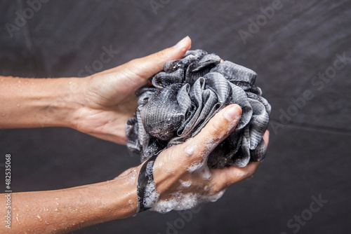 a woman's hand holds a black loofah as it suds up with soap and bubbles in a black tile shower photo