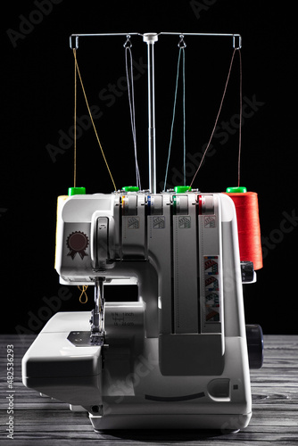 Professional overlock sewing machine with multicolored thread on a dark background photo