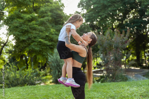 Fototapeta Naklejka Na Ścianę i Meble -  Maternal love and care. Fit mom holds her little daughter in her arms in the park. Healthy lifestyle, fitness