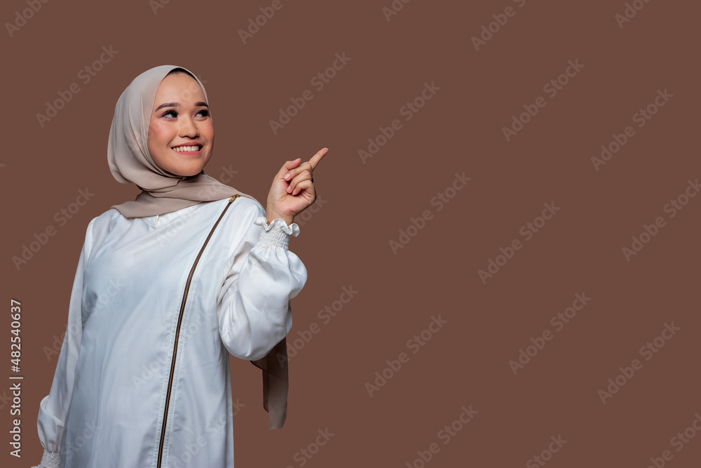 Beautiful woman in hijab is pointing to the right side with smile expression isolated on plain background Beautiful woman in hijab is pointing to the right side with smile expression isolated on plain background