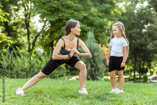 Mom trainer shows technique of doing the exercise her little daughter. Active family concept