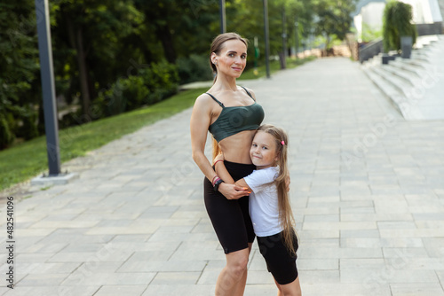 Little daughter hugs fit mom outdoors. Love concept, active family, fitness