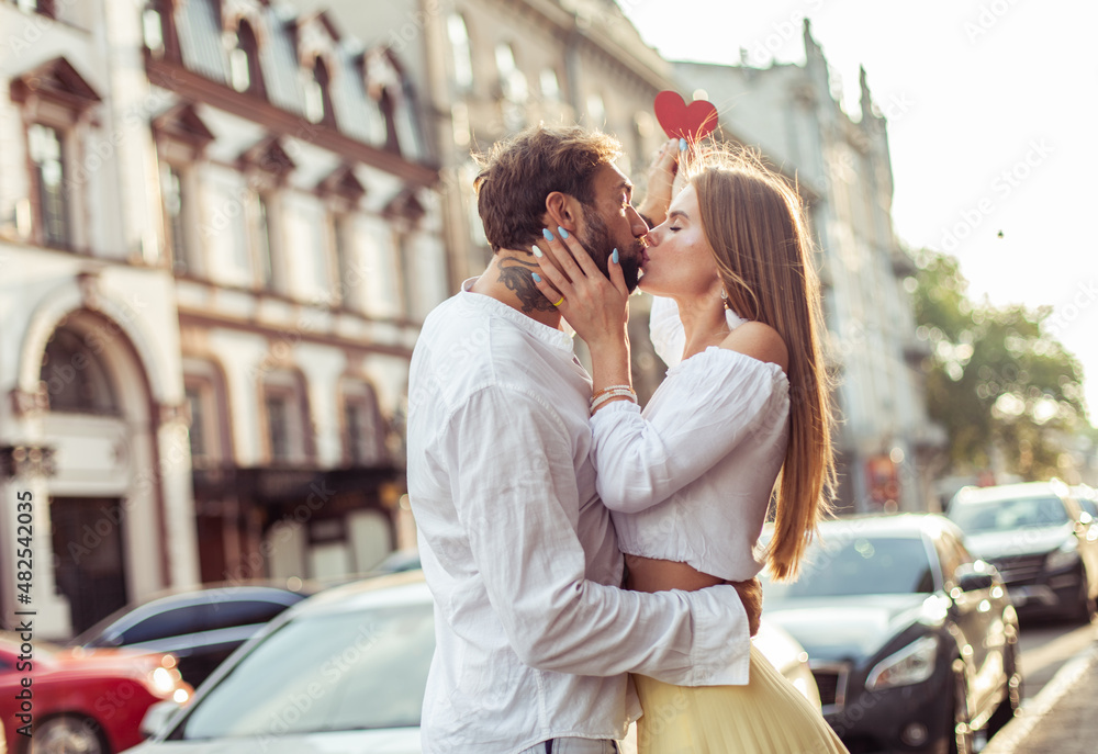 Young couple in love hold a red heart, show their love and kiss in the city. Romantic concept Young couple in love hold a red heart, show their love and kiss in the city. Romantic concept