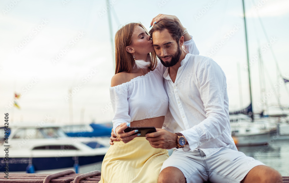Beautiful couple in love spend time together and watch video on smartphone in yacht club