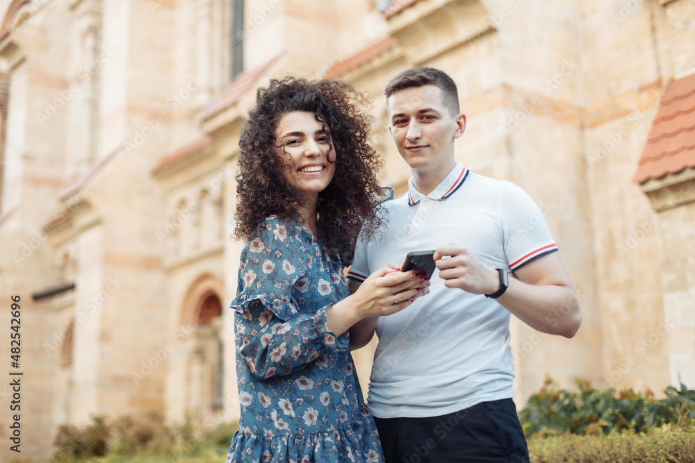 Naklejka premium Cute young couple use smartphone against city architecture background. Travel, lifestyle concept