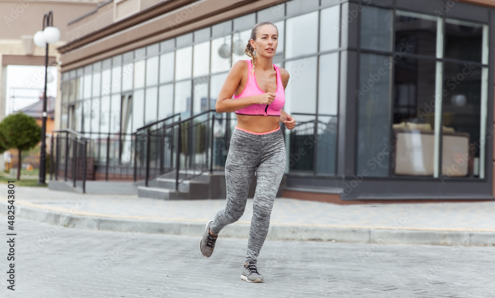 Young woman in overalls runs on in sports clothes outdoors