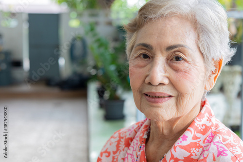 Close up shot with copy space of asian senior female (80 years old) with gray hairs who is looking and smiling to camera with happy face and beautiful eyes for her enjoy retirement life. photo