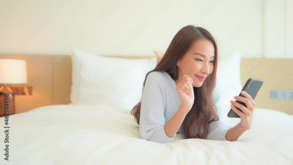 Young asian female on bed celebrating win on bet or bid while looking at mobile phone, full frame Young asian female on bed celebrating win on bet or bid while looking at mobile phone, full frame