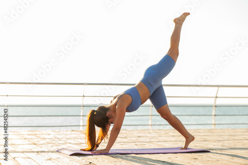 Young woman in sportswear practicing yoga on yoga mat on beach