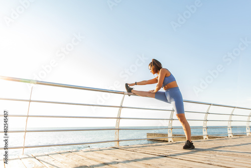 Fit woman practicing leg stretching on the beach. Active lifestyle