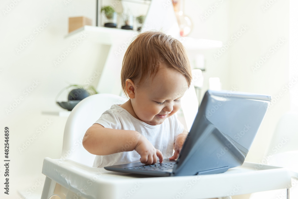 Little funny baby girl typing on a netbook while sitting at the children's table at home Little funny baby girl typing on a netbook while sitting at the children's table at home