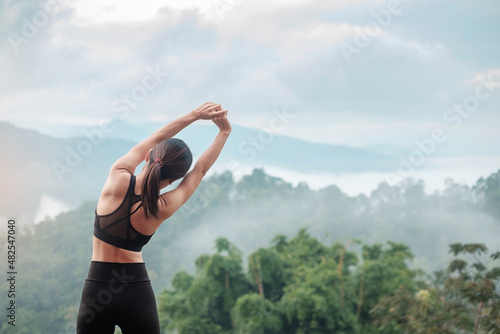 Young fitness female in sportswear stretching body against mountain view, healthy woman exercise in morning. Workout, wellbeing and work life balance concepts