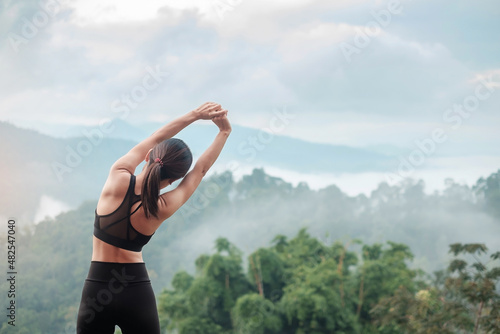 Young fitness female in sportswear stretching body against mountain view, healthy woman exercise in morning. Workout, wellbeing and work life balance concepts photo