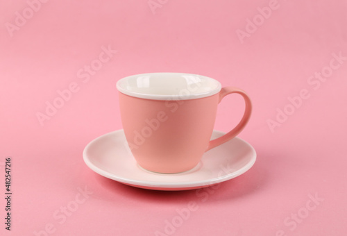 Empty ceramic cup and saucer on pink background