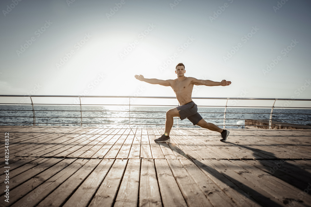 Fototapeta premium Young muscular man practicing yoga asana at sunrise on the beach