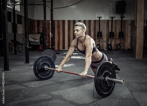 Muscular woman training mishtsi press with barbell in modern gym