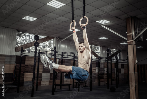 Muscular male gymnast exercising on gymnastic rings in a modern health club. Healthy lifestyle concept