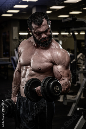 strong young bearded caucasian muscular man lifting heavy dumbbells in sport gym during fitness bodybuilding workout training