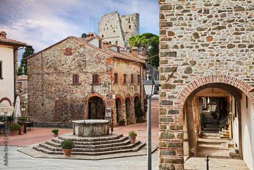 Fototapeta Naklejka Na Ścianę i Meble -  Civitella in Val di Chiana, Arezzo, Tuscany, Italy: the square of the village with ancient buildings with porticoes, the well and water cistern, the ruins of the medieval castle on background