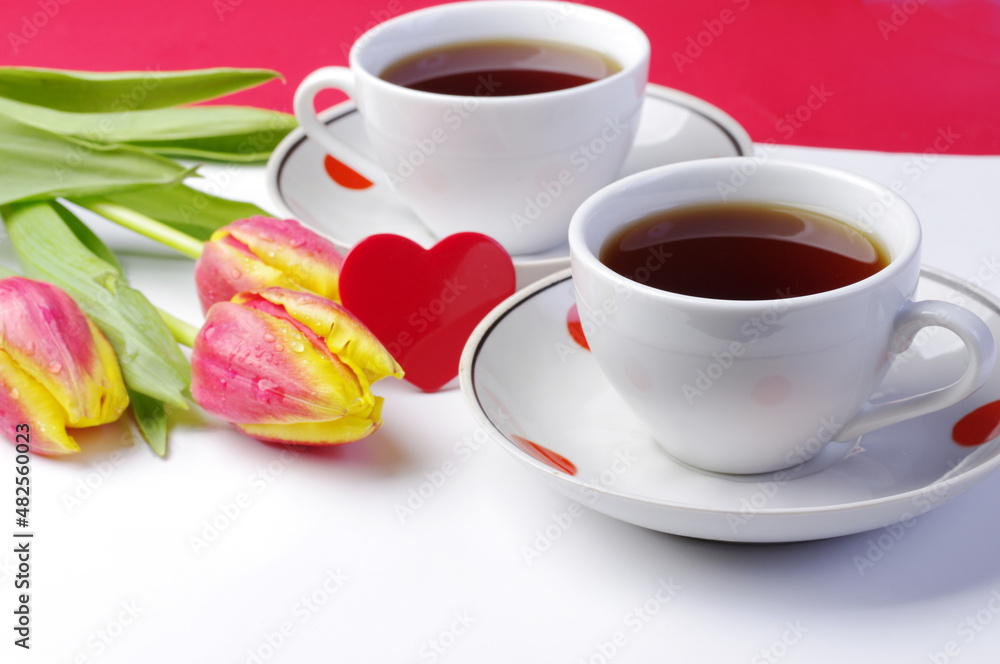 Two cups of tea, a red heart and a bouquet of tulips on the table.