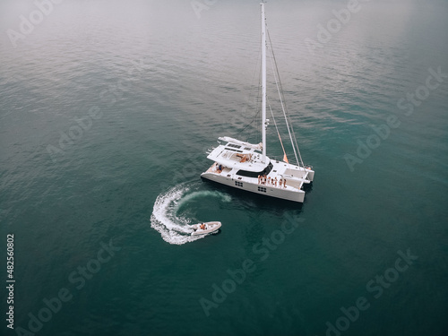A nice aerial view of a white yacht with several young handsome girls in swimsuits looking at a guy in a cap on a white motoboat.Looking for driving. Luxury party style. The concept of holiday.