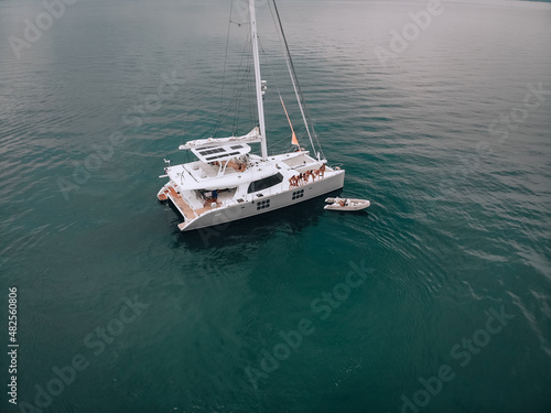 A wonderful photo from the copter of a white yacht with several pretty young nice girls in swimsuits watching at a guy on a white motorship. Drive to the swimming equipments. The concept of leisure.