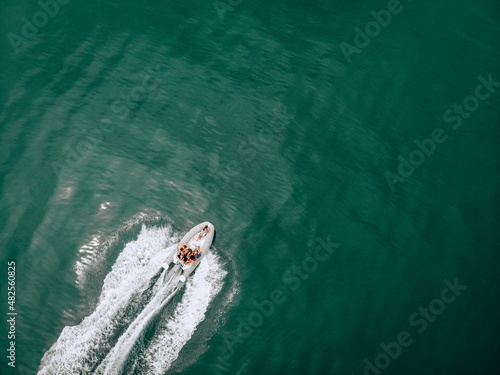 Photo from the drone. Photo session on a white motorboat on the turquoise sea. A guy with a professional camera takes pictures of young cute girls in swimsuits. The concept of an exciting photoshoot. © Semachkovsky 