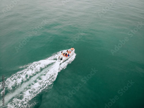 Drone's image in open space at sea. Young people sail on a white motor boat on a hot summer day. Beautiful young womens in swimsuits communicate with a guy in a black cap and a camera in his hands. © Semachkovsky 