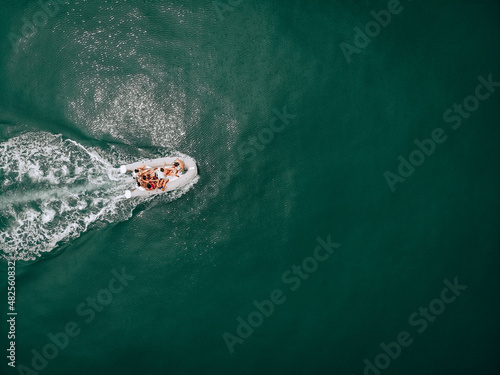 Beautiful summer copter's photo. Party of young people on a white boat. Fun riding of girls in swimsuits with a guy in black cap. Turquoise traces of waves from the motor. Hot summer day concept.