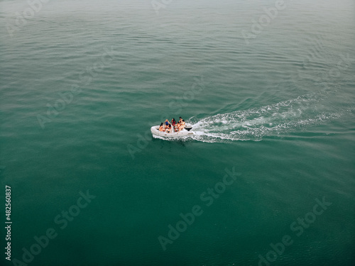 An excellent photo of sitting young people riding on a motorboat in the open turquoise sea. The guy controls the vehicle. Girls have fun. The concept of having entertainments. © Semachkovsky 