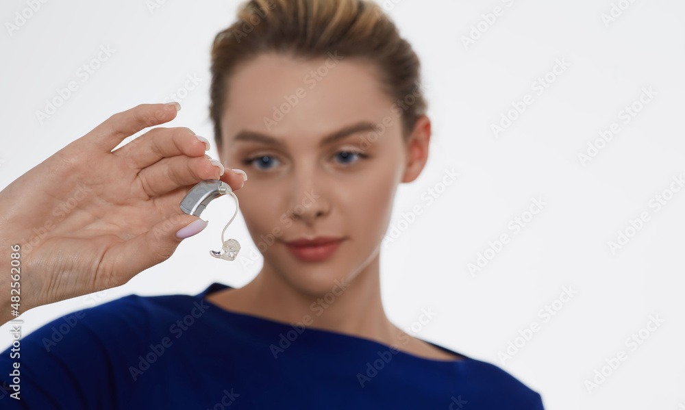 Treatment of deafness in adult people, hearing solutions. Beautiful woman holding latest generation hearing aid in her hand on foreground Treatment of deafness in adult people, hearing solutions. Beautiful woman holding latest generation hearing aid in her hand on foreground