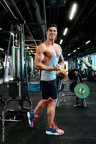 Professional healthy trainer and certified trainer working out. Portrait of muscular attractive man working out at gym, doing biceps muscle training and flexing muscles.