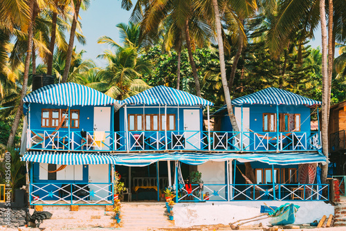 Canacona, Goa, India. Famous Painted Guest Houses On Palolem Beach Against Background Of Tall Palm Trees In Sunny Day.Canacona, Goa, India. Famous Painted Guest Houses On Palolem Beach Against